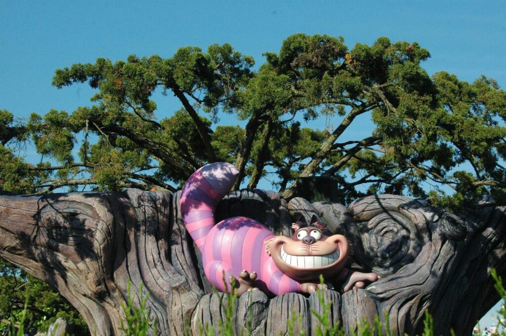 Cheshire Cat statue perched on a whimsical tree with clear blue sky.