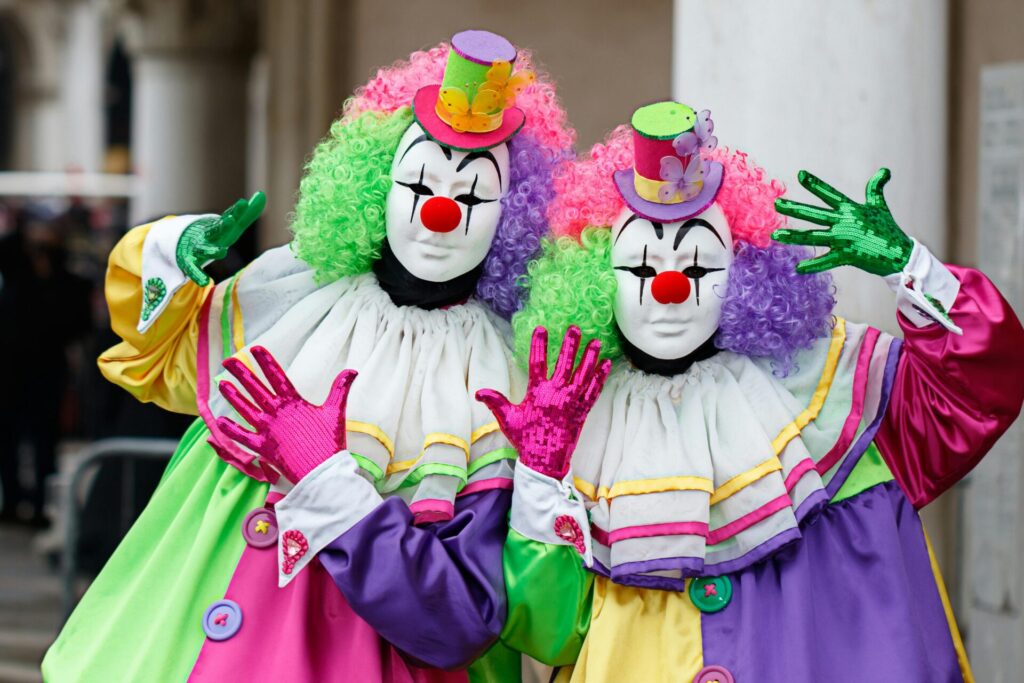 Two clowns in colorful costumes and makeup posing for a portrait, showcasing vibrant and playful fashion.